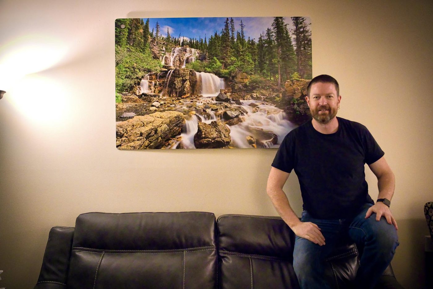 Micheal Lander sitting beside a 24 by 36 inch brushed aluminum print of the Tangle Creek waterfall hanging on a living room wall